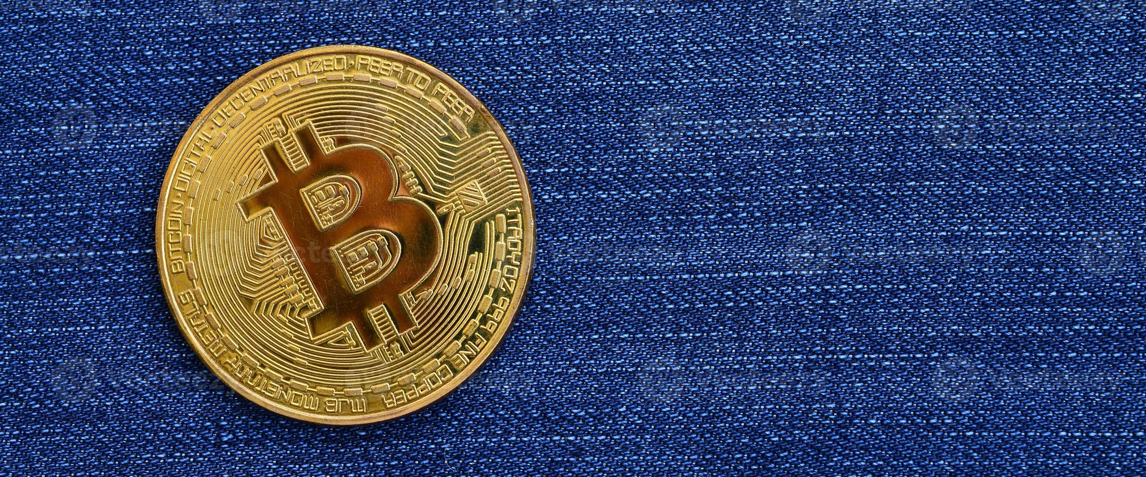 Golden Bitcoin lies on a blue jeans fabric. New virtual money. New crypto currency in the form of the coins photo