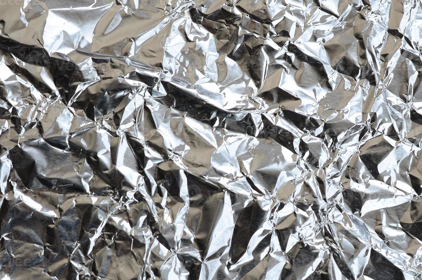 Thin wrinkled sheet of crushed tin aluminum silver foil background with shiny crumpled surface for texture photo