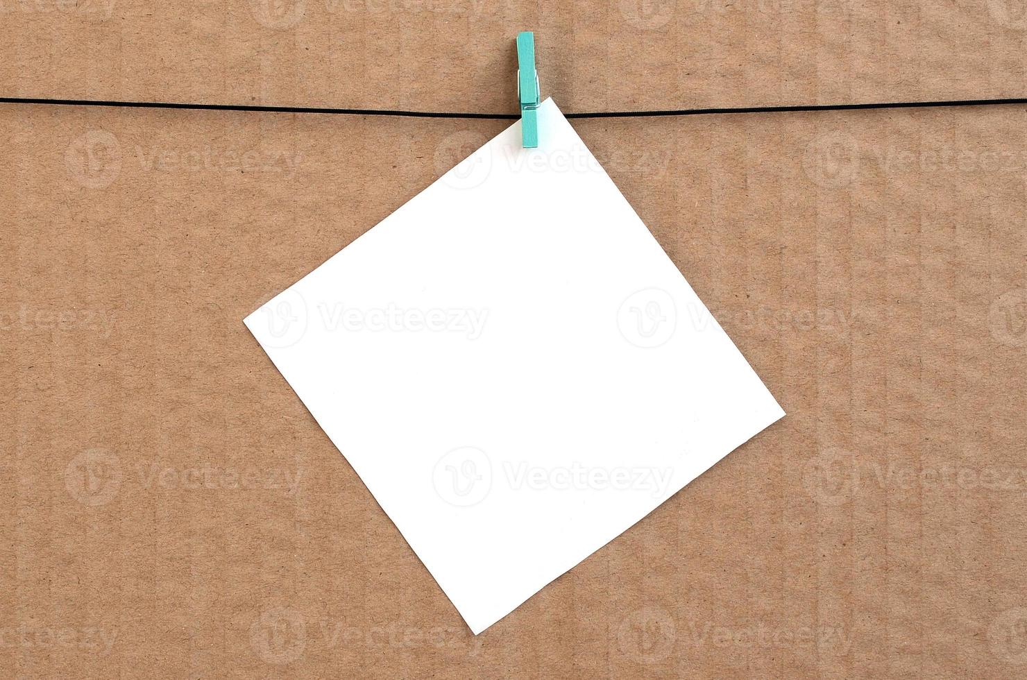 White blank card on rope on a brown cardboard background. Creative reminder, small sheet of paper on wooden clothespin, memo backdrop photo