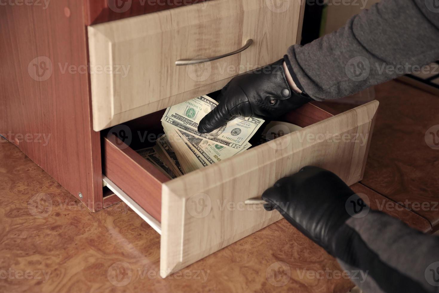 ladrón con traje negro y guantes se ve en un estante abierto en la cocina. el ladrón saca los billetes de dólar estadounidense de un estante foto