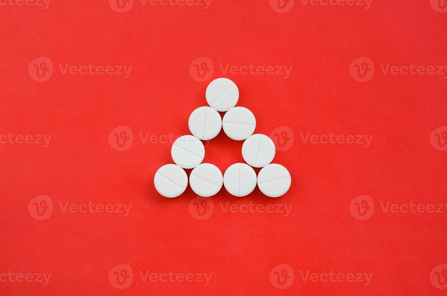 Several white tablets lie on a bright red background in the form of an even triangle. Background image on medicine and pharmaceutical topics photo