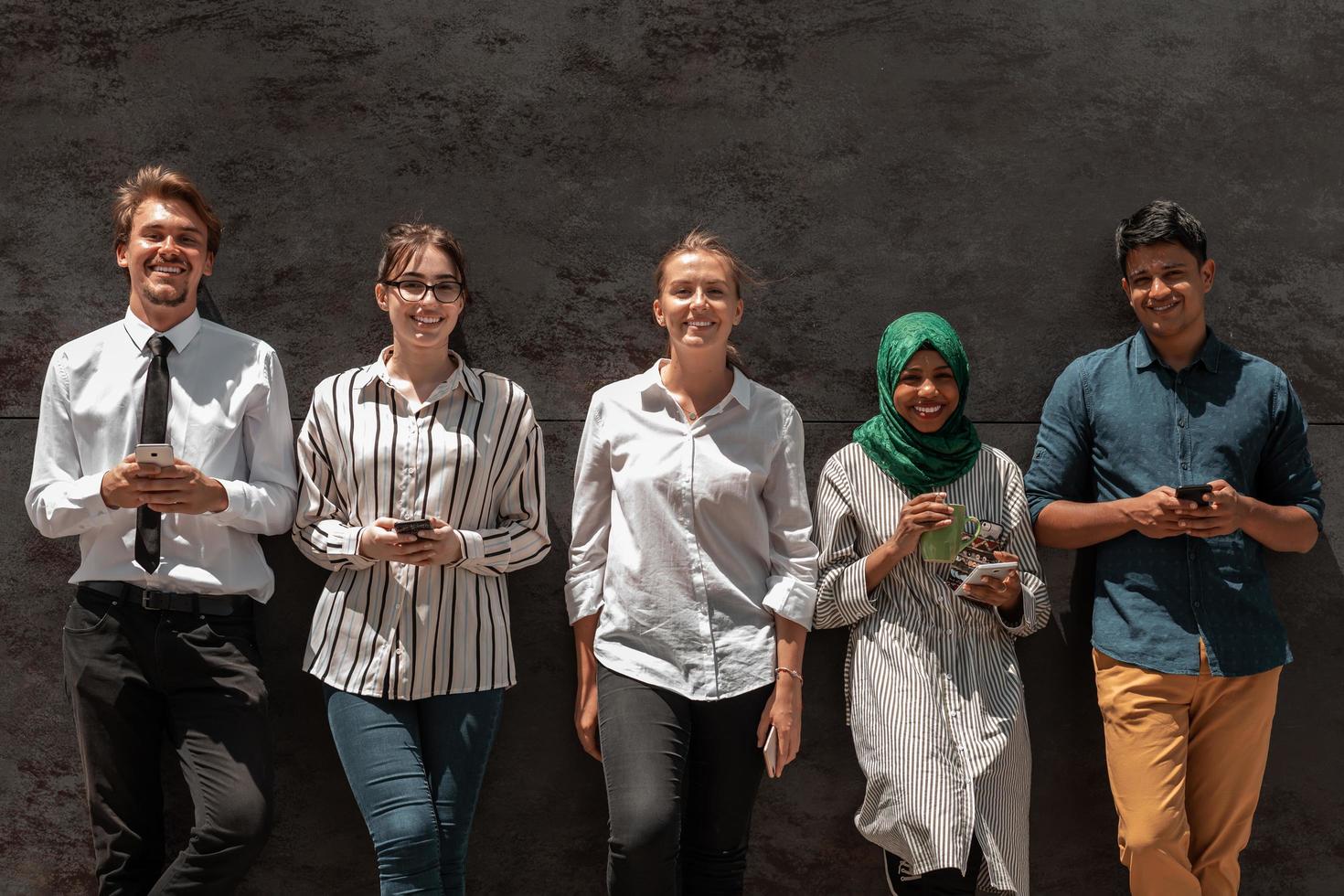 Multiethnic group of casual business people using mobile phone during coffee break from work in front of black wall outside photo