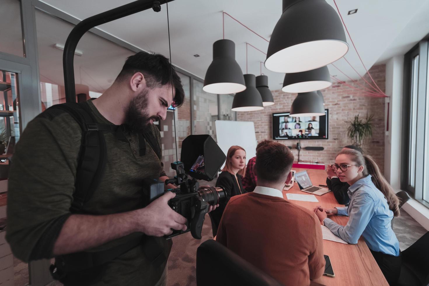 Behind the scene. Cameraman recording a group of young multiethnic business people working and communicating together in a creative office. Selective focus photo