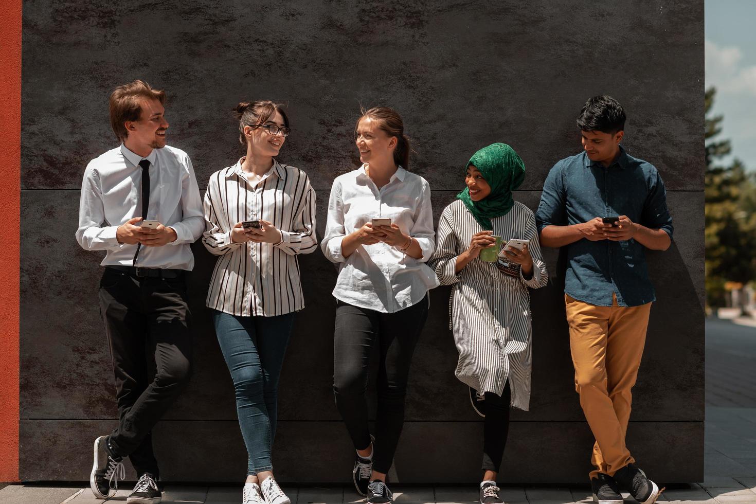 Multiethnic group of casual business people using mobile phone during coffee break from work in front of black wall outside photo