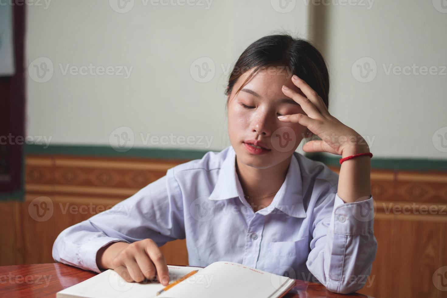 una estudiante que usa la camiseta blanca está cansada de su estudio y hace su tarea, tiene un problema con la lección difícil en casa, la educación y el espacio de copia del concepto de examen para el diseño de texto individual foto