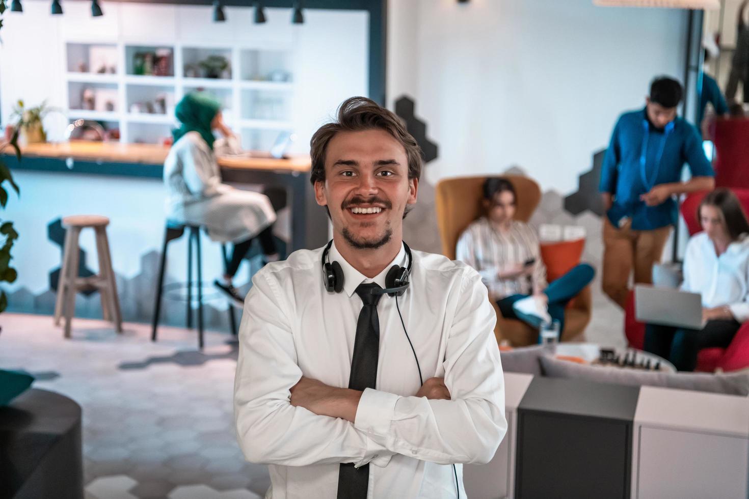 Portrait of successful businessman entrepreneur with headphones around his neck and colleagues in the background at busy startup office photo