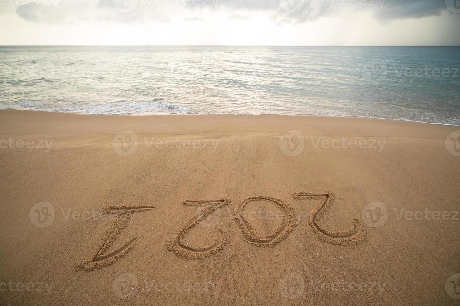 Handwriting year 2021 on sand and foam wave on beach. photo