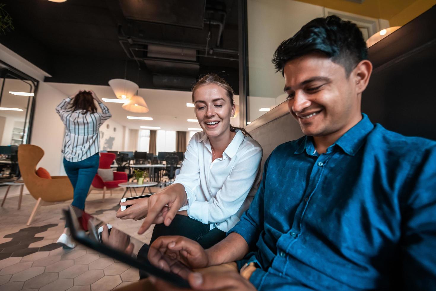 Multiethnic business people man with a female colleague working together on tablet computer in relaxation area of modern startup office photo