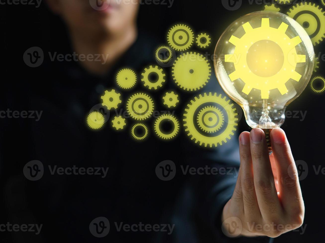 Hand holding light bulb and Innovation gears connection icon inside. Idea and inspiration on black background. photo