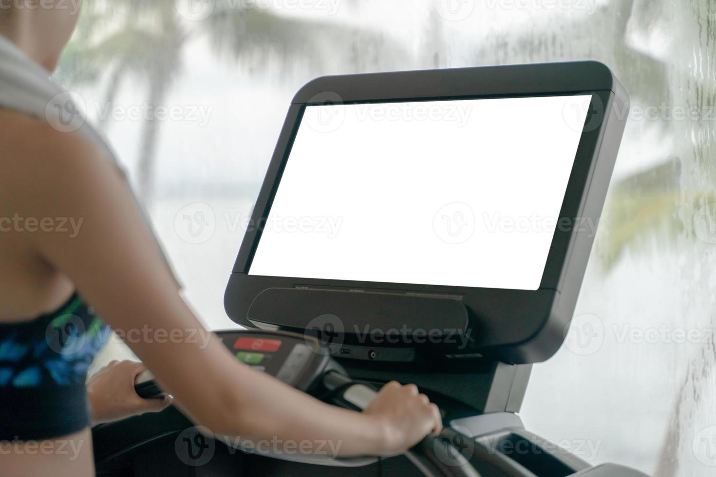 la mujer está trabajando en el gimnasio. haciendo entrenamiento cardiovascular en cinta rodante con maqueta de pantalla blanca, grandes ventanales con vista al mar lloviendo afuera. foto