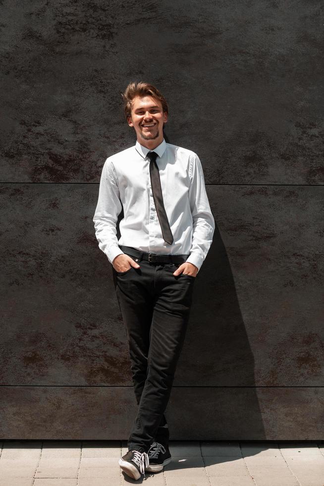 Portrait of startup businessman in a white shirt with a black tie standing in front of gray wall outside photo