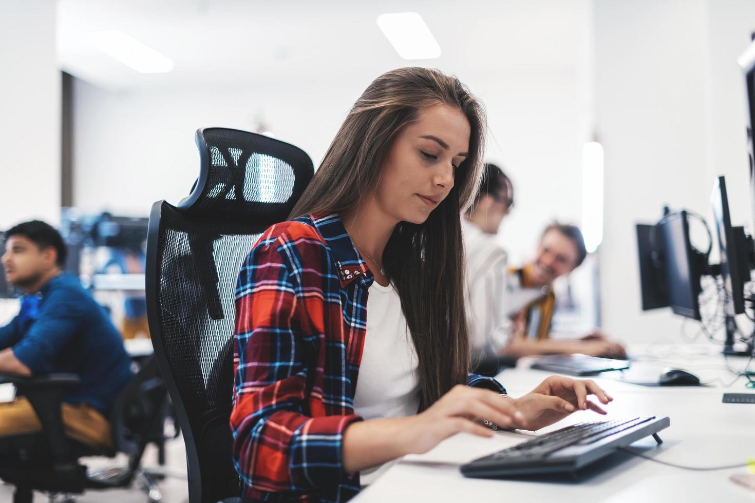 Casual business woman working on desktop computer in modern open plan startup office interior. Selective focus photo