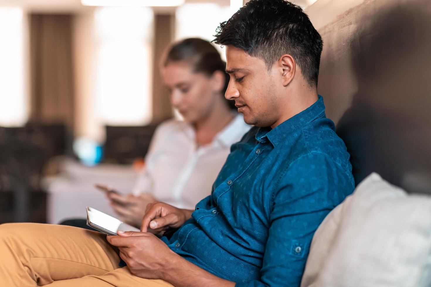Multiethnic business people man with a female colleague working together on tablet computer in relaxation area of modern startup office photo