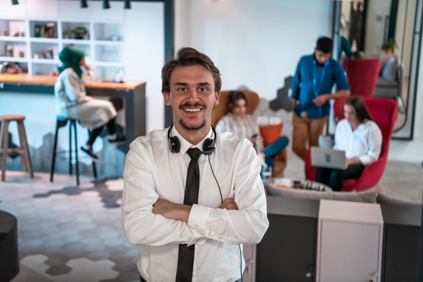 retrato de un exitoso empresario con auriculares alrededor del cuello y colegas en segundo plano en una oficina de inicio ocupada foto