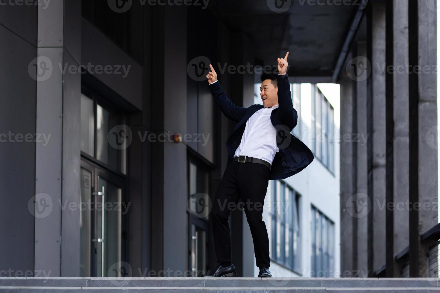 Happy and cheerful Asian businessman dancing near the office rejoices in victory and success photo