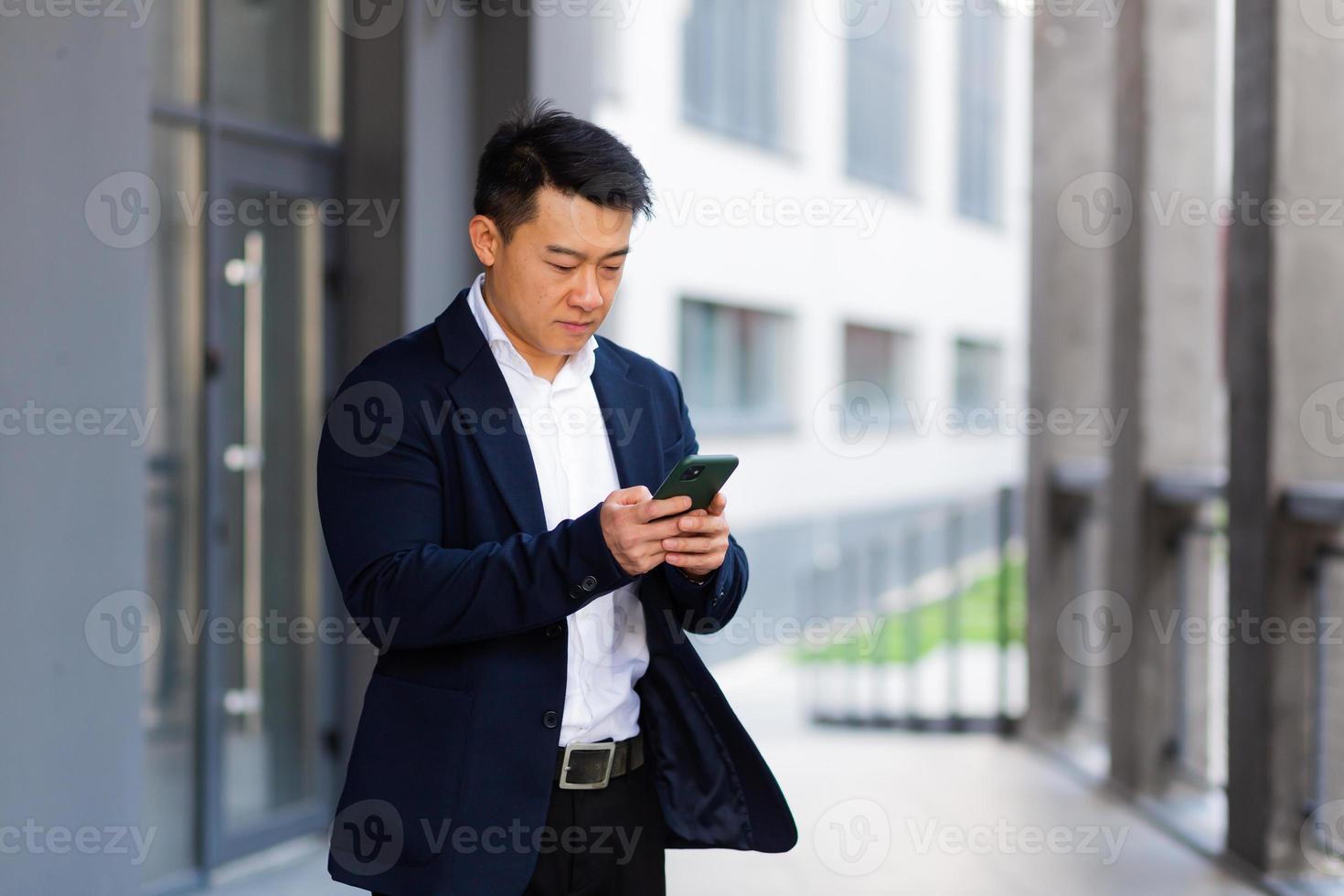 el jefe de negocios asiático mira el teléfono móvil lee noticias del teléfono y escribe i foto