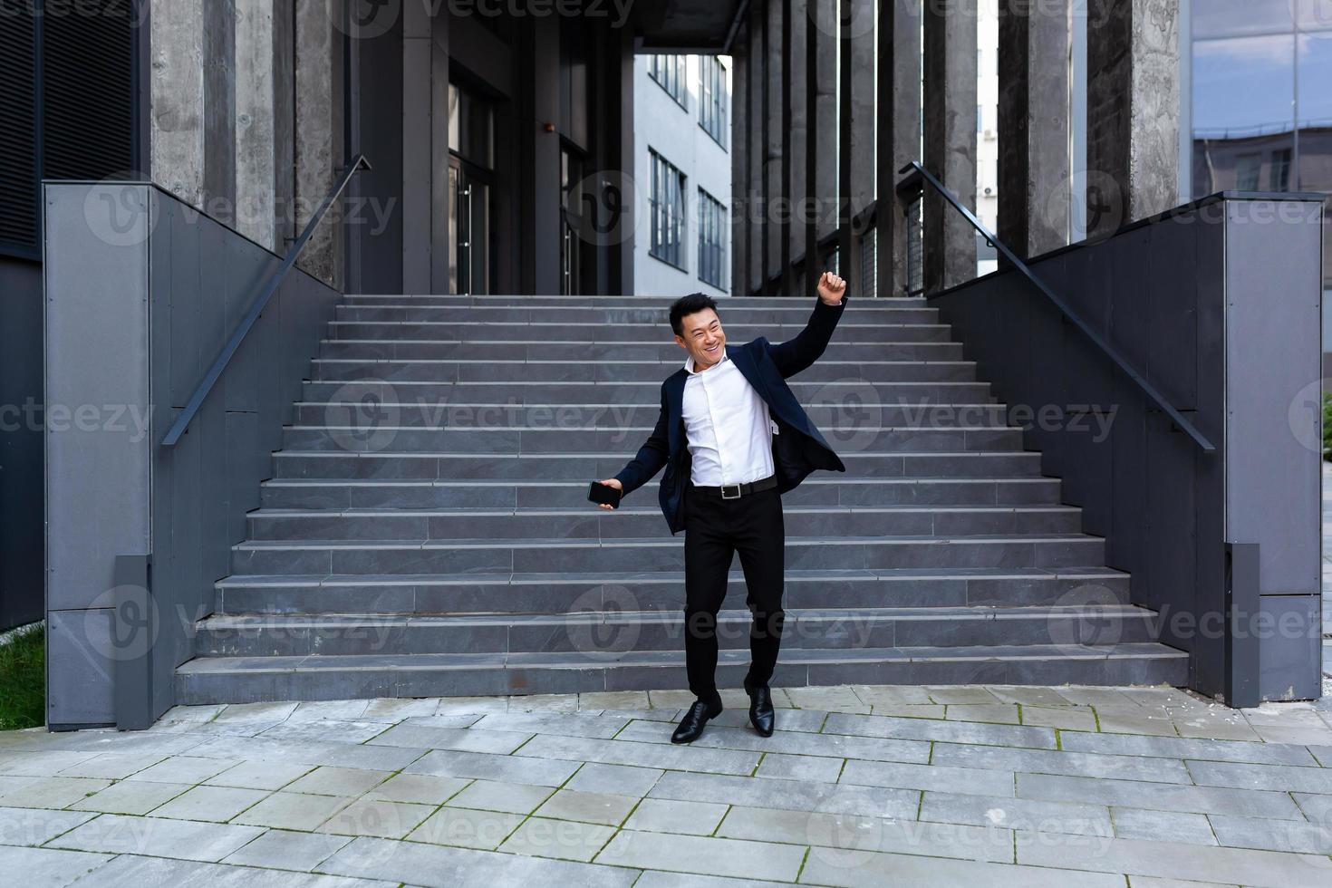 Happy and cheerful Asian businessman dancing near the office rejoices in victory and success photo