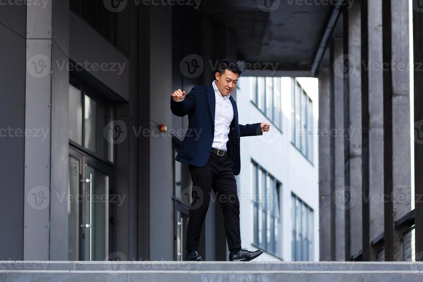 feliz y alegre hombre de negocios asiático bailando cerca de la oficina se regocija en la victoria y el éxito foto