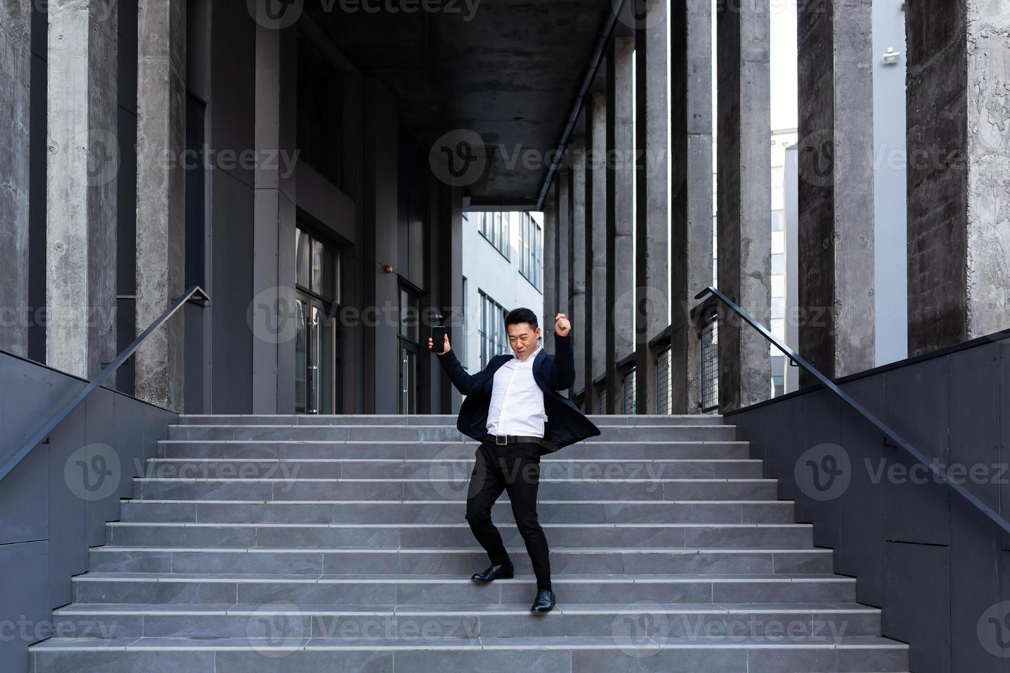 Happy and cheerful Asian businessman dancing near the office rejoices in victory and success photo