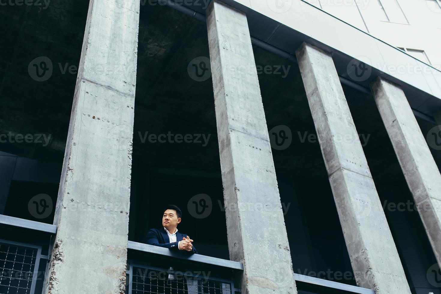 joven empresario asiático de pie cerca de un moderno edificio de oficinas negro hecho de hormigón foto