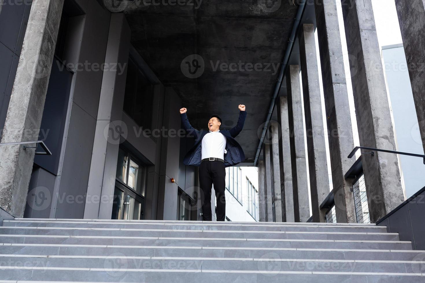 Happy and cheerful asian businessman holding hands up rejoicing in victory and success photo