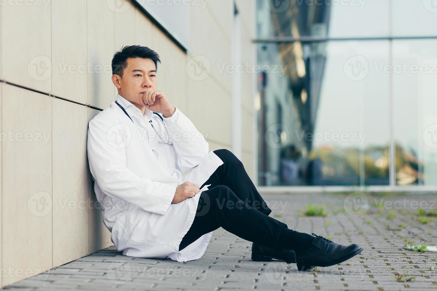 portrait Doctor Asian man tired after work sitting on the floor near the clinic disappointed photo