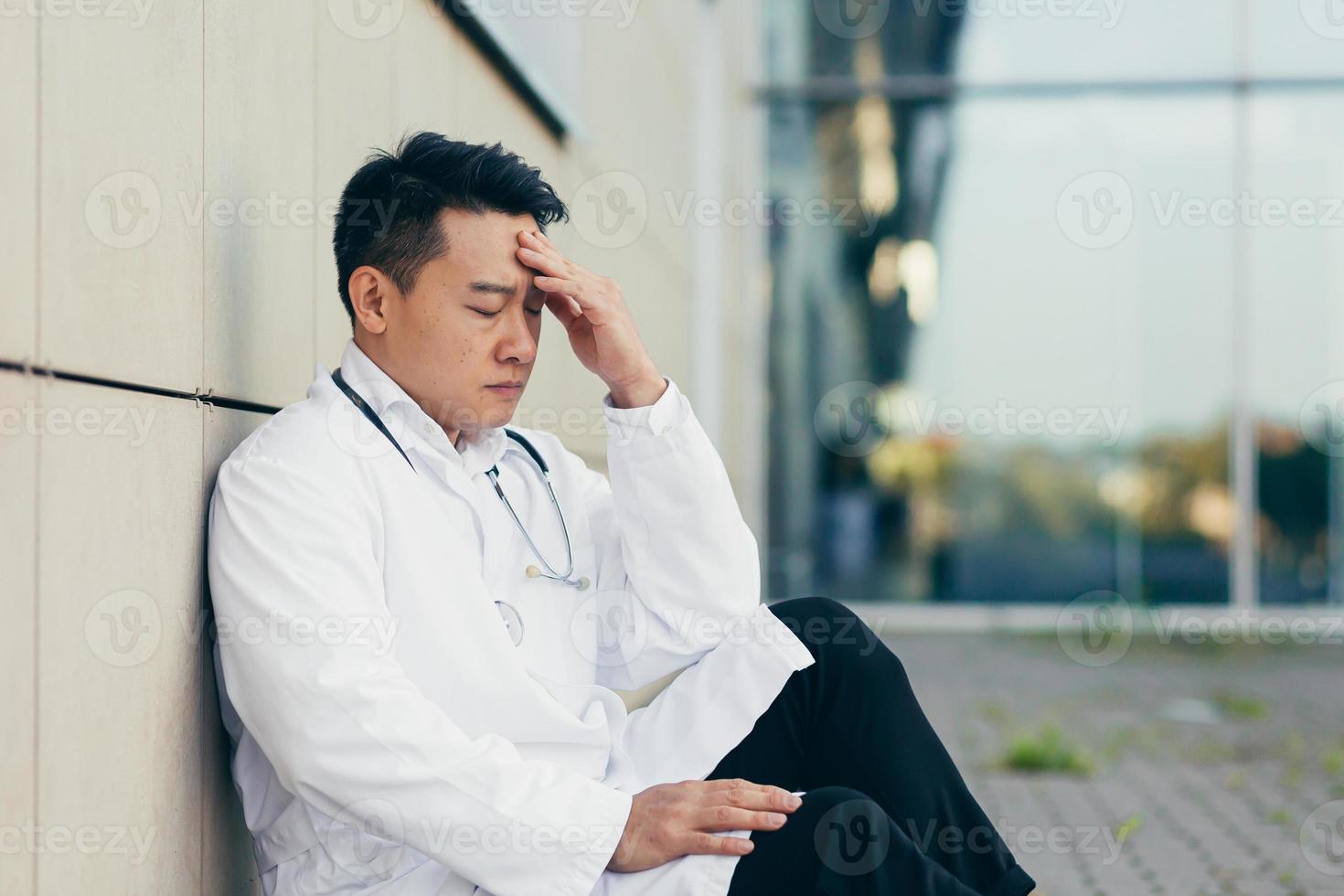 portrait Doctor Asian man tired after work sitting on the floor near the clinic disappointed photo