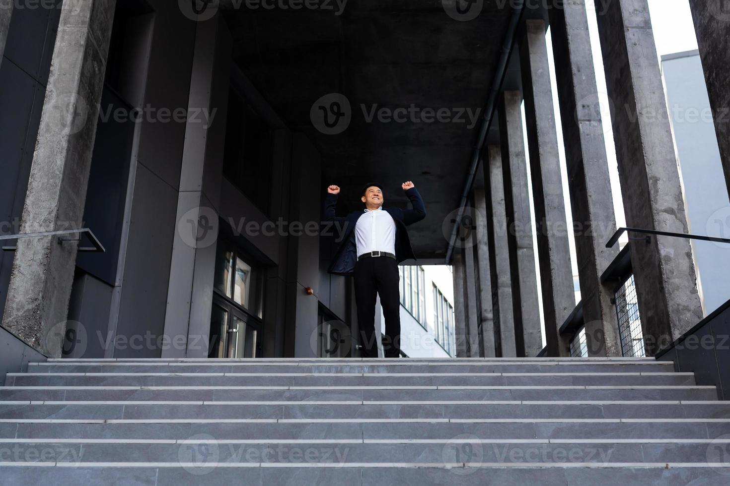 Happy and cheerful asian businessman holding hands up rejoicing in victory and success photo