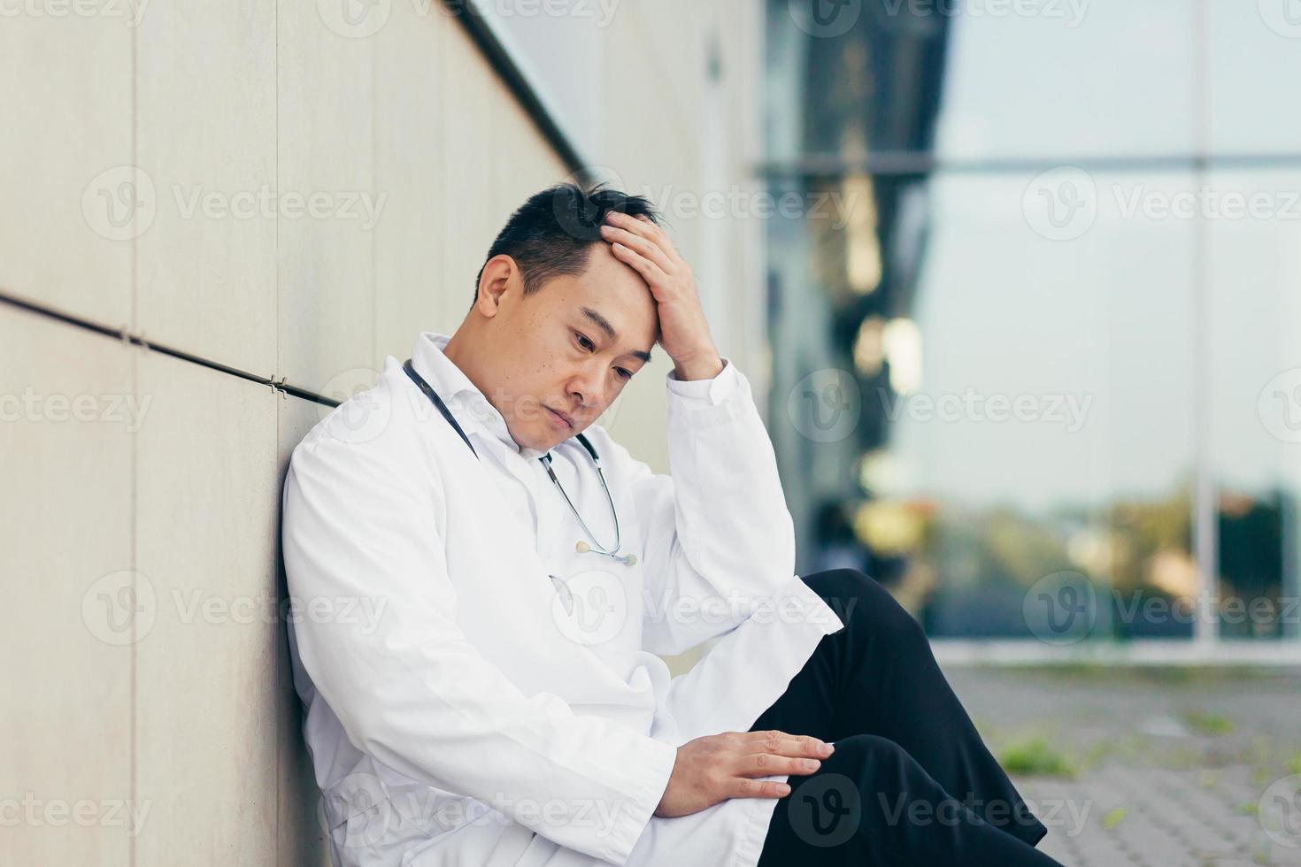 portrait Doctor Asian man tired after work sitting on the floor near the clinic disappointed photo