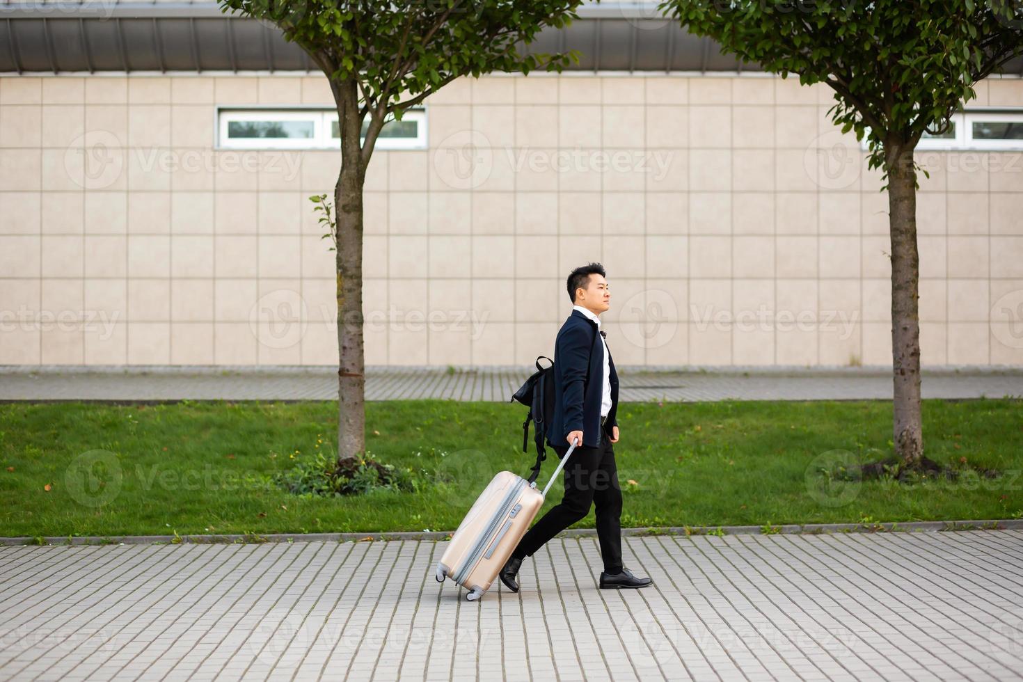 Successful asian businessman near airport and bus station goes with suitcases serious photo