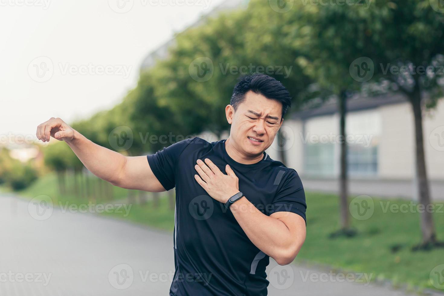 Male asian athlete, kneading shoulder pain, sore arm muscles in the park photo