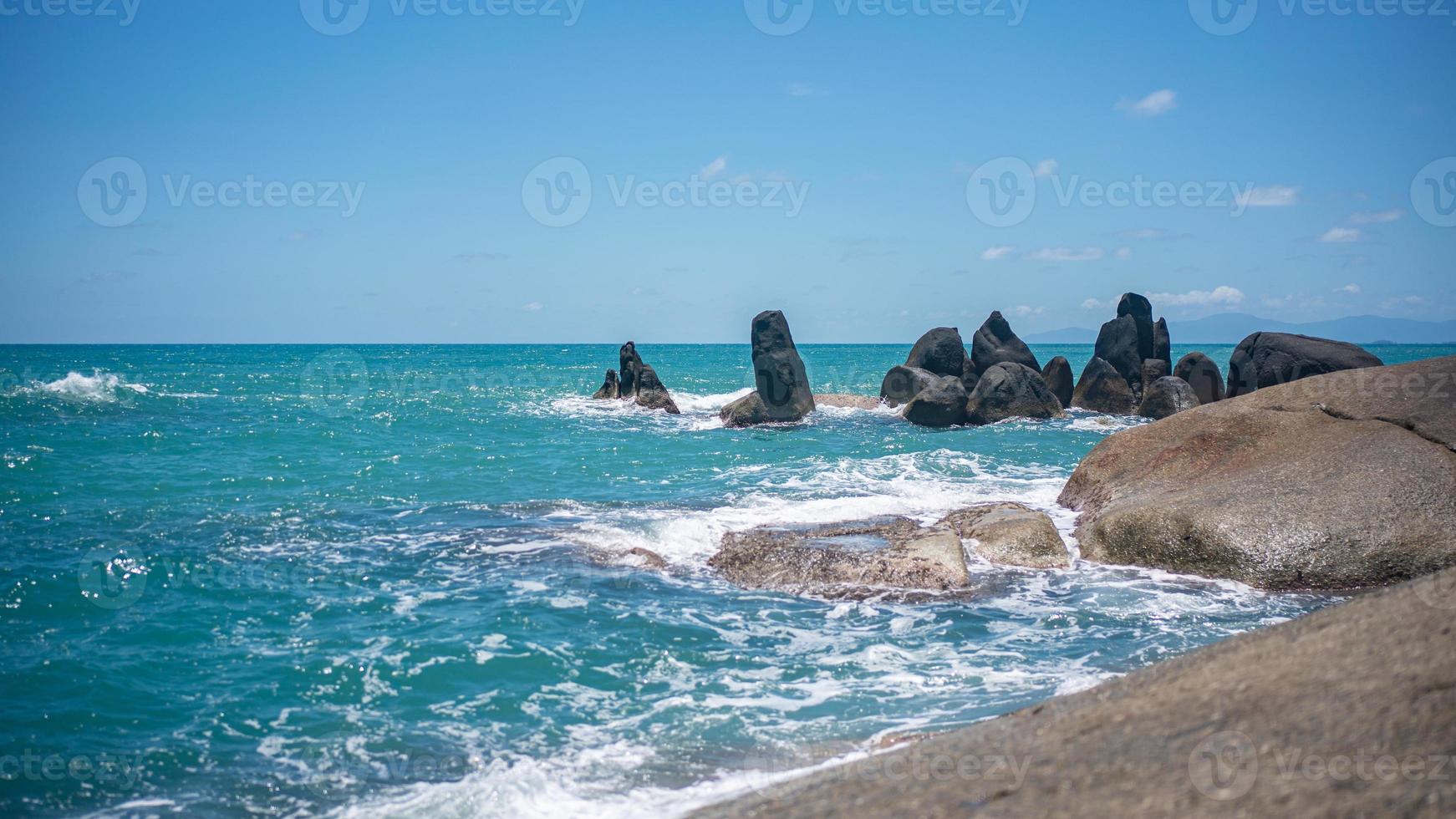 Rocky beach with white waves, deep blue ocean views and blue sky. photo