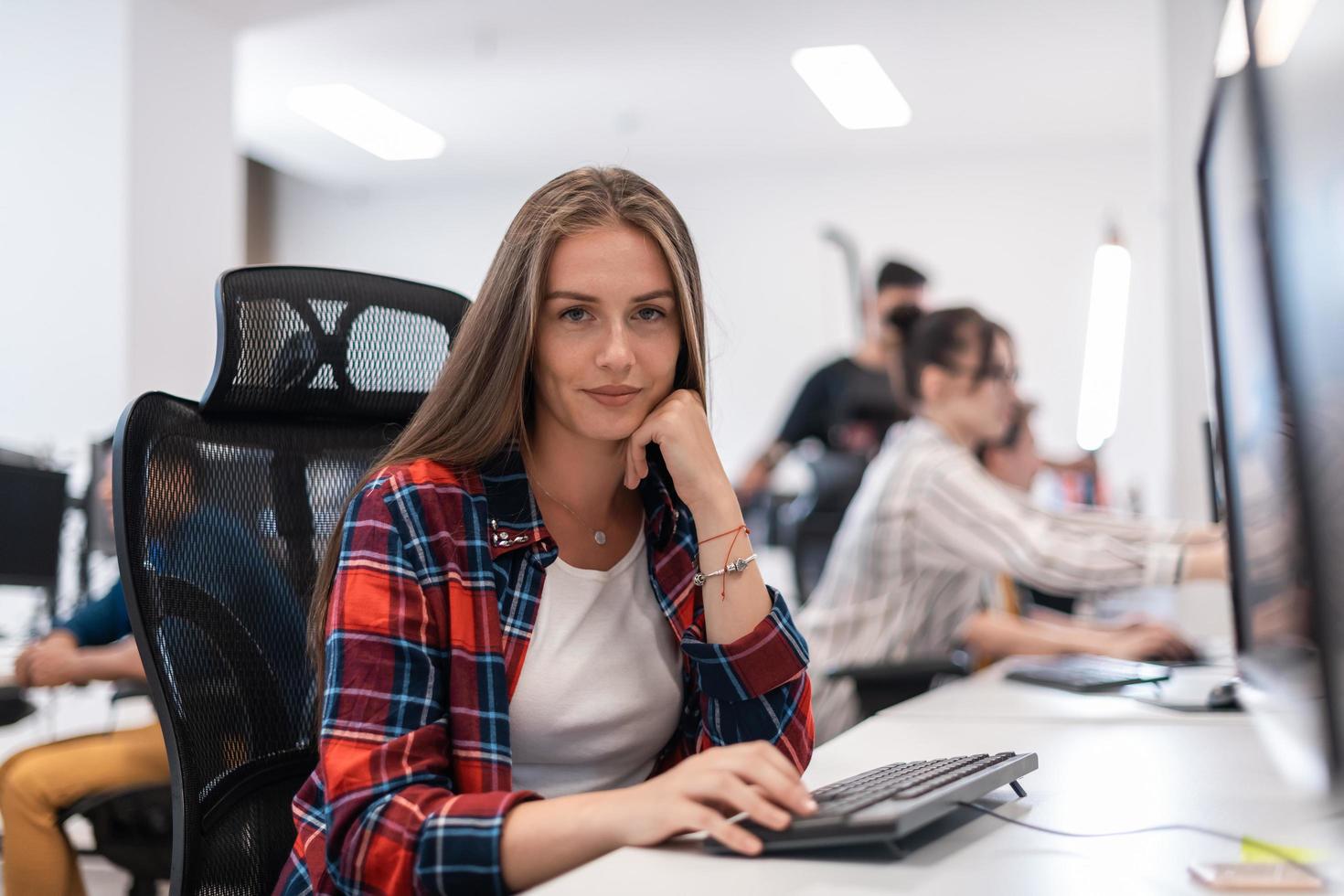 Casual business woman working on desktop computer in modern open plan startup office interior. Selective focus photo