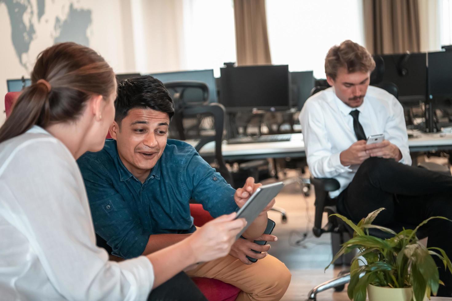 equipo de negocios multiétnico que tiene una lluvia de ideas en el área de relajación del interior de la oficina moderna que trabaja en una computadora portátil y una tableta foto