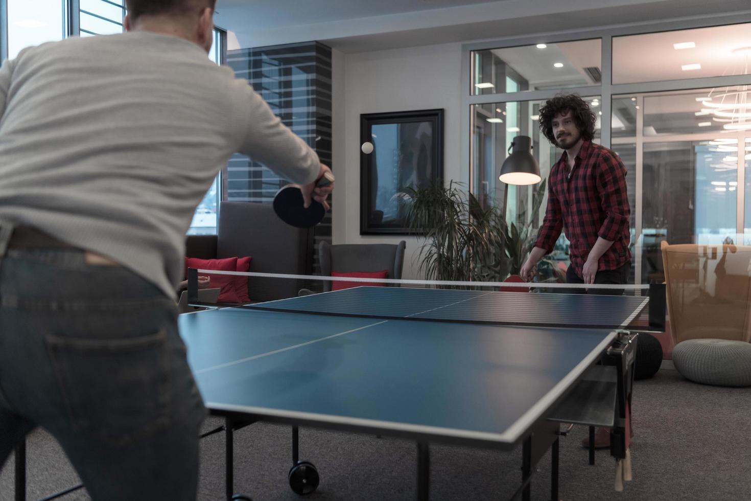 Two young start up business man playing ping pong tennis at modern creative office space people group have meeting and brainstorming in background photo