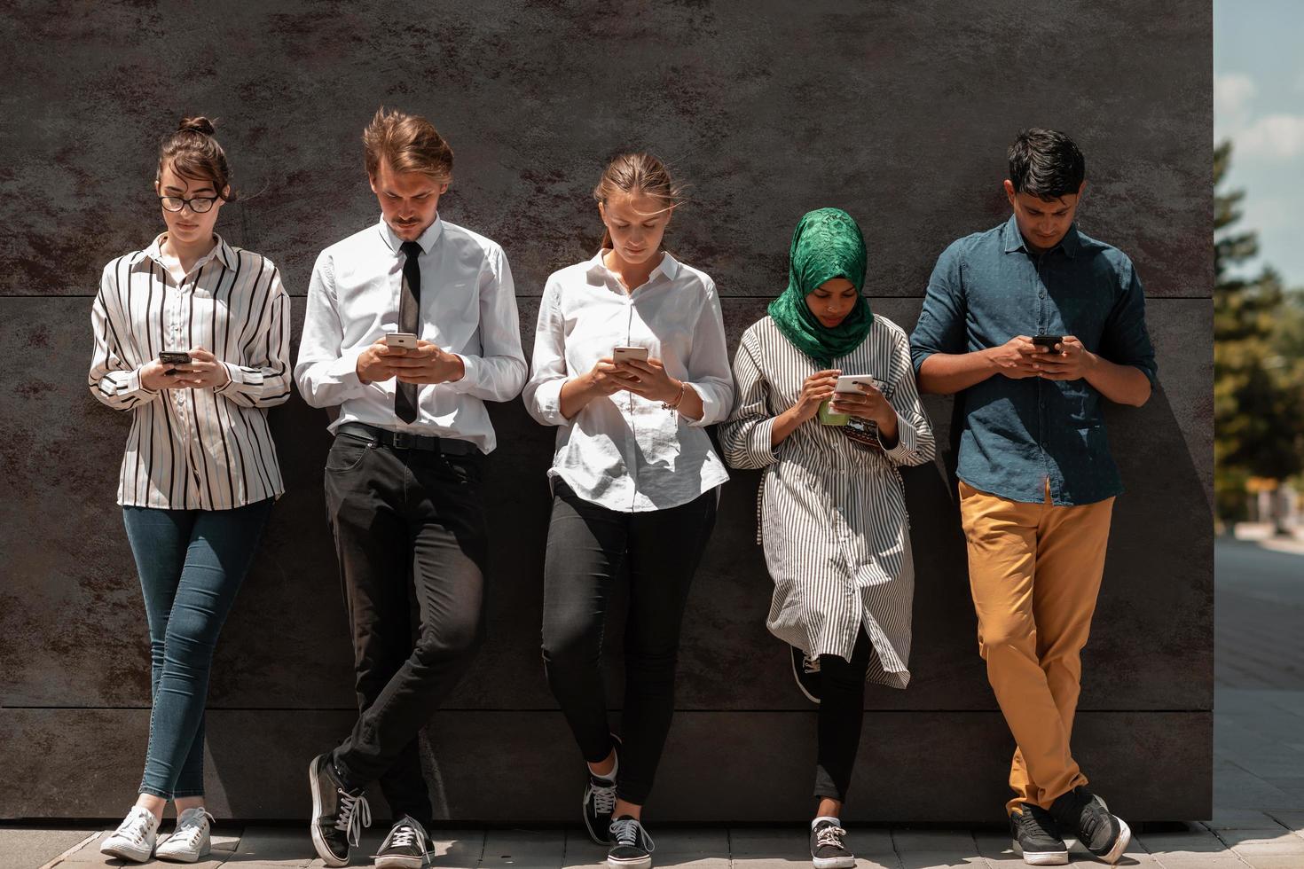 Multiethnic group of casual business people using mobile phone during coffee break from work in front of black wall outside photo