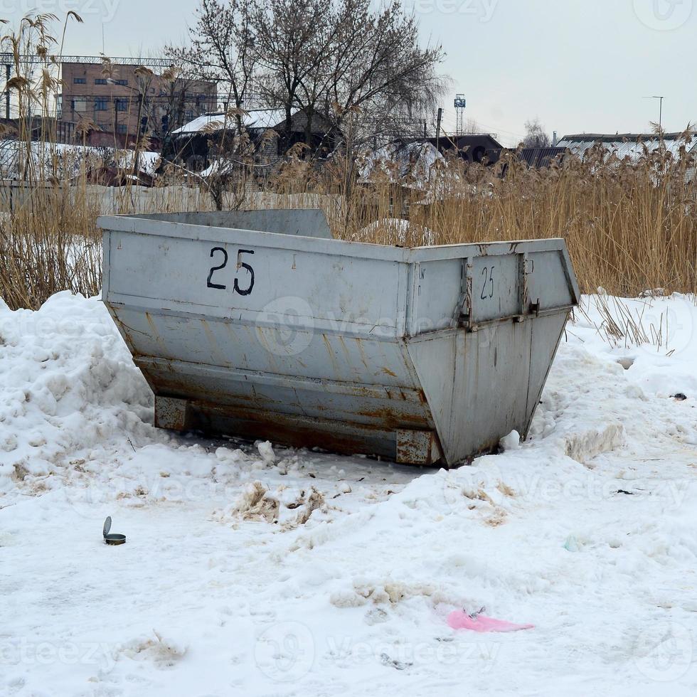 Trash bin at the side of street in winter with lip garbage container winter snow. Metal container for household waste photo