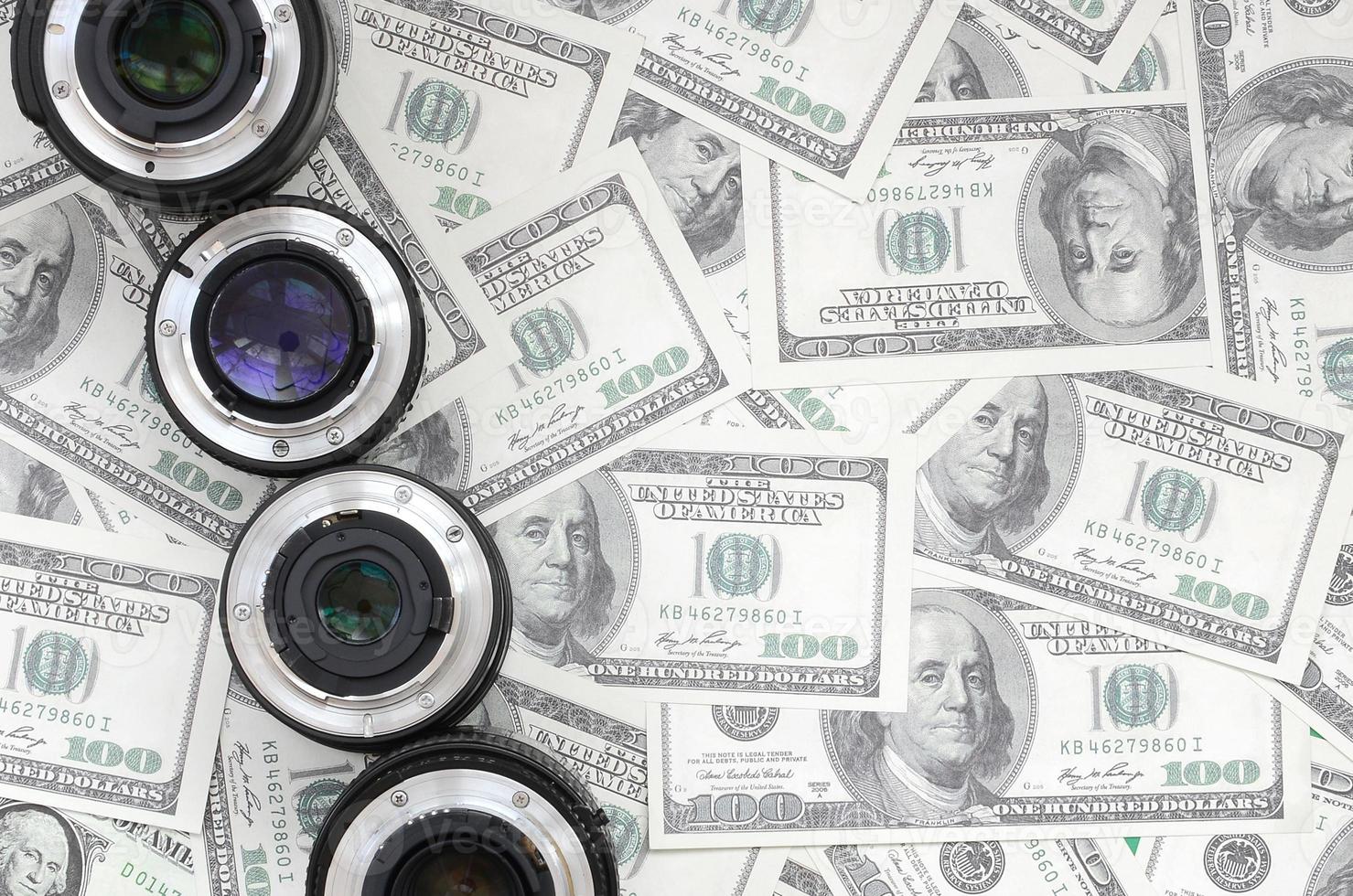 A few photographic lenses lies on the background of a lot of dollar bills. Space for text photo