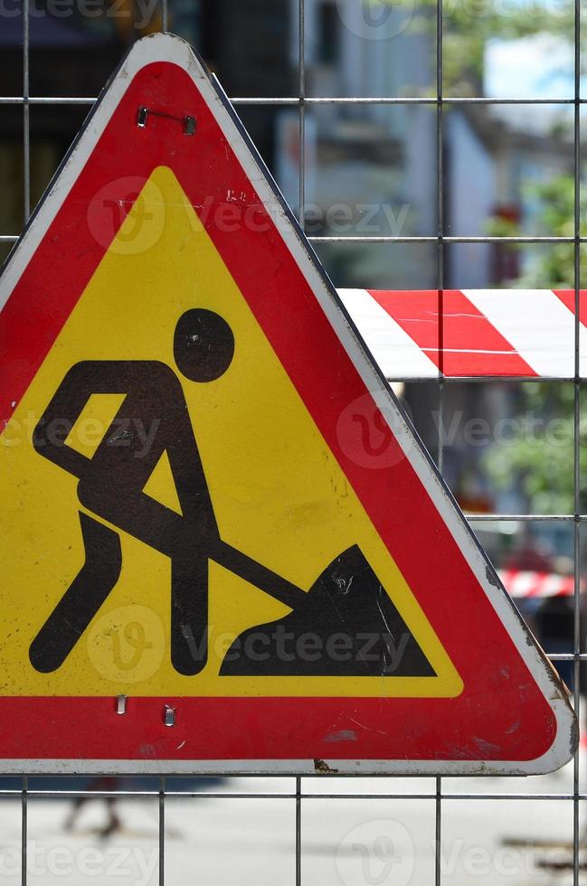 The warning sign under construction is attached to a metal mesh fence with a red and white striped signal tape photo