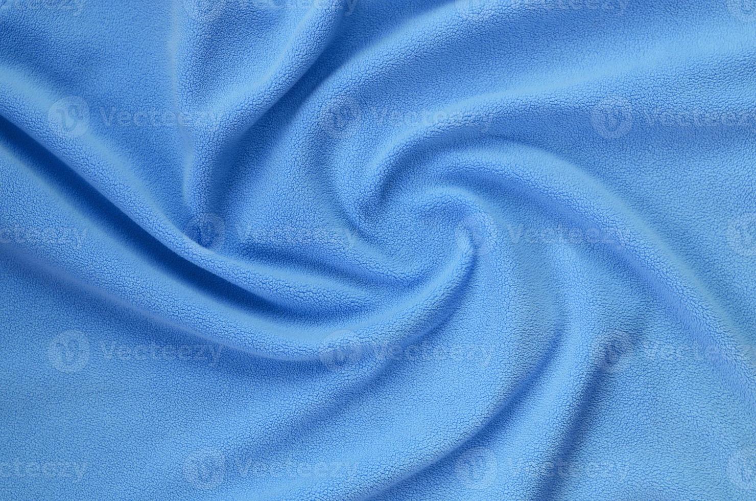 The blanket of furry blue fleece fabric. A background of light blue soft plush fleece material with a lot of relief folds photo