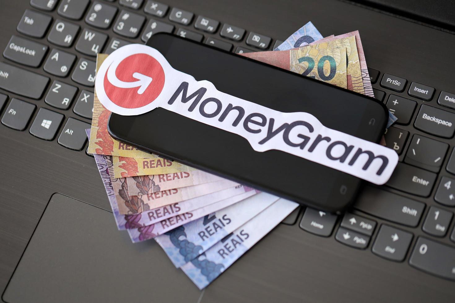 TERNOPIL, UKRAINE - SEPTEMBER 6, 2022 MoneyGram paper logotype lies on black laptop with brazilian reals. Moneygram is American cross border P2P payments and money transfer company photo