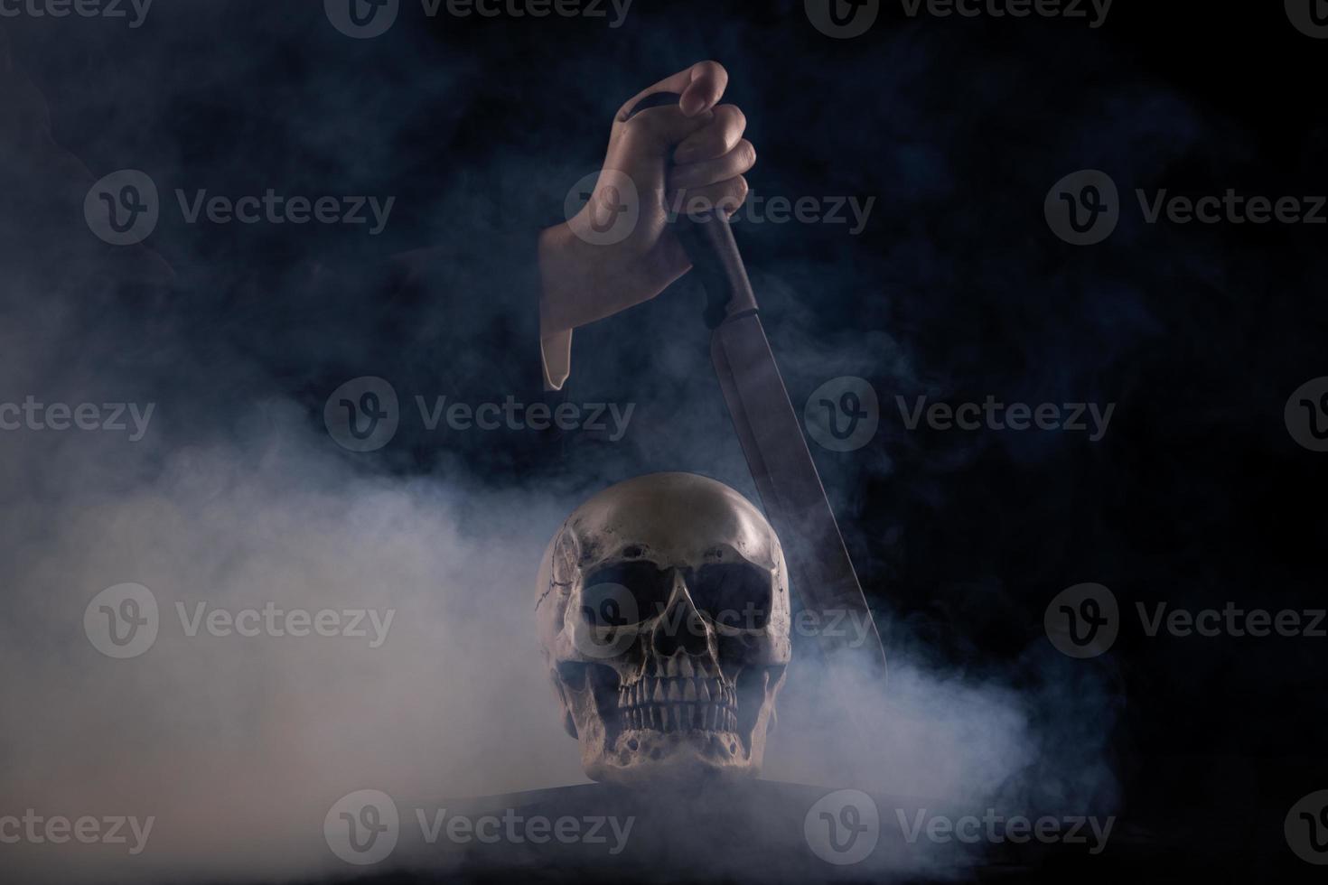 cráneo humano de halloween en una vieja mesa de madera sobre fondo negro. forma de hueso del cráneo para la cabeza de la muerte en el festival de halloween que muestra el cuchillo asesino mata la sentencia muerta, copia el espacio foto