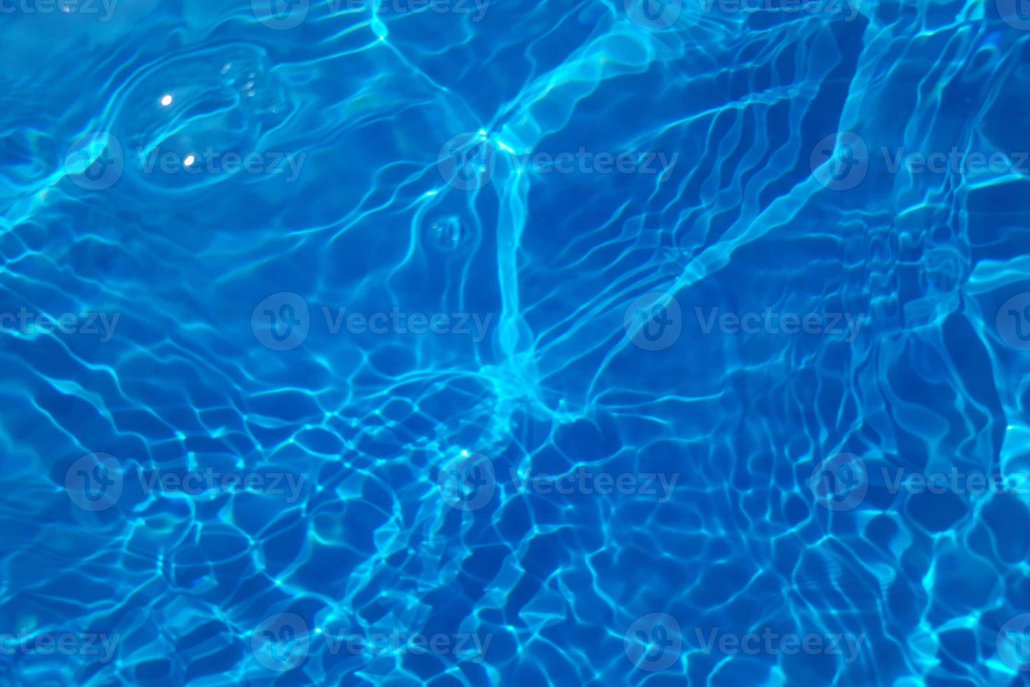 Defocus blurred transparent blue colored clear calm water surface texture with splash, bubble. Shining blue water ripple background. Surface of water in swimming pool. Blue bubble water shining. photo
