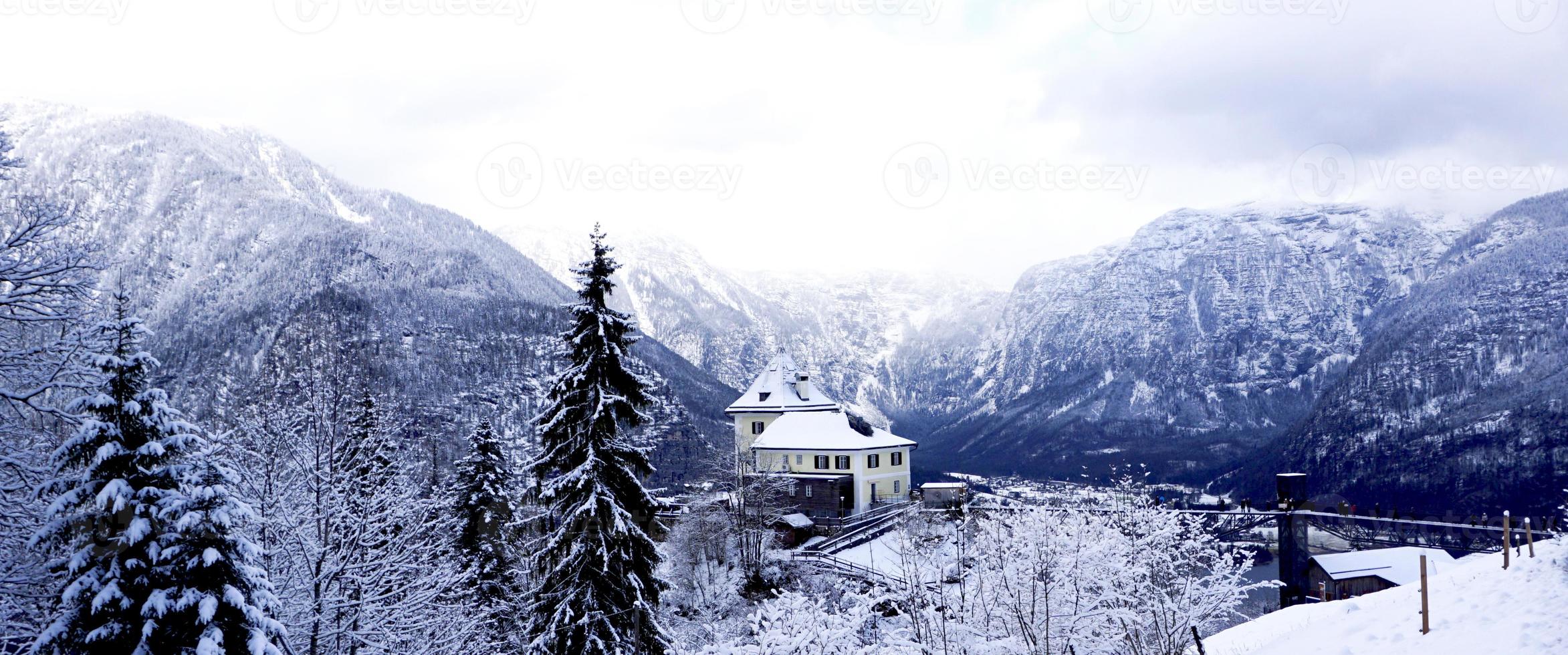 panorama del paisaje de montaña de nieve de invierno de hallstatt a través del bosque foto