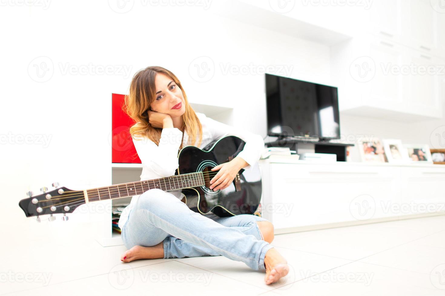 Beautiful woman in home sitting on the floor with her left-handed guitar photo