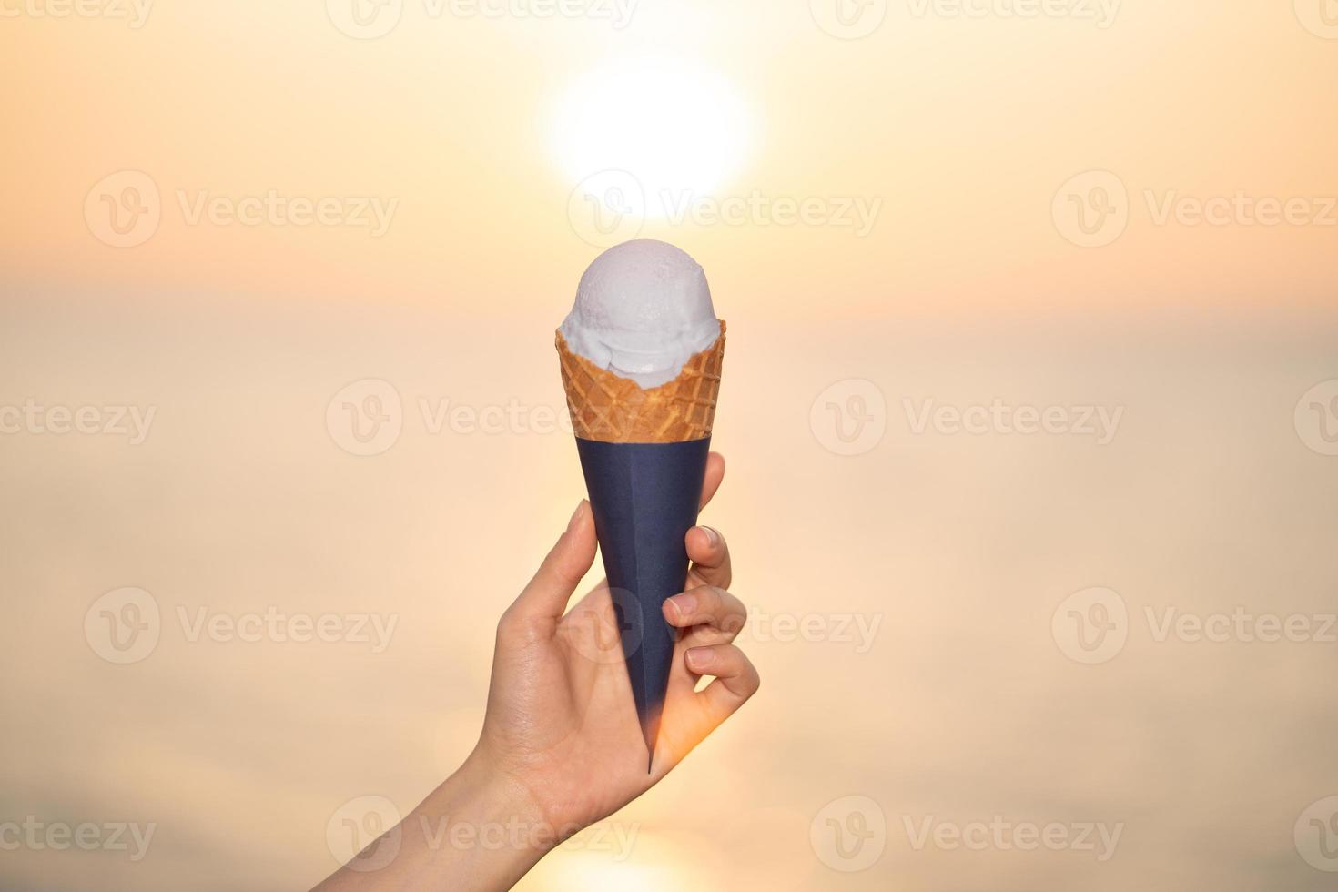 Scoop ice cream with a waffle cone in hand on the beach, sunset moment. photo