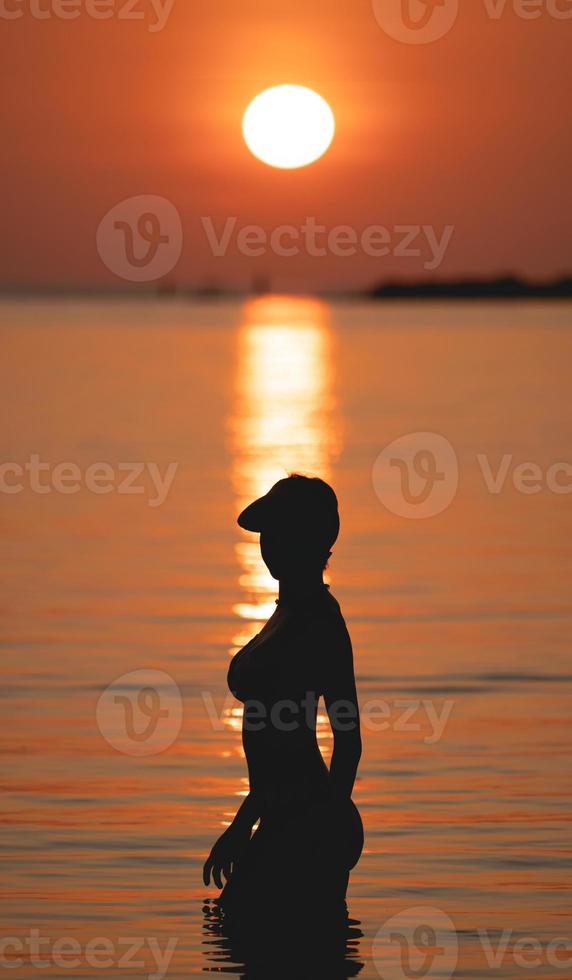 Sunset ocean view. Sun above the sea on orange sky. Woman standing on beach. photo