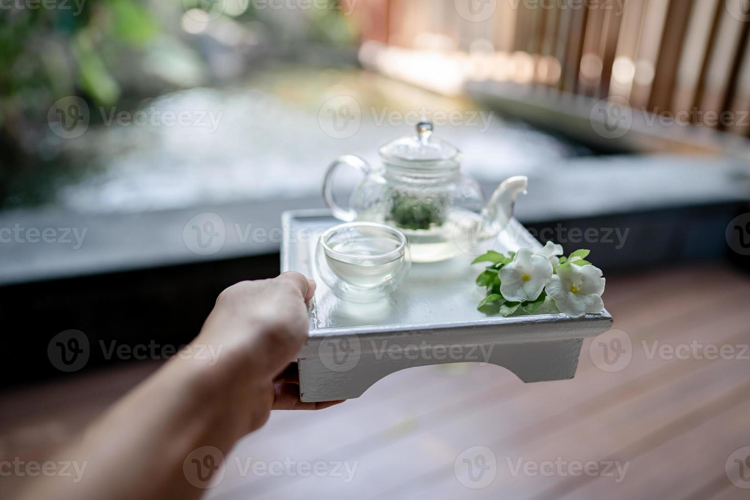 Hand holding the tray served transparent teapot with herbal tea. photo