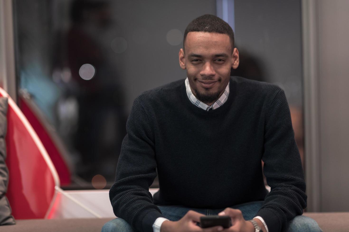 Young African American work in coworking space using smartphone analyzing online market trends, focused man worker reading financial news or browsing internet on phone. Technology concept photo