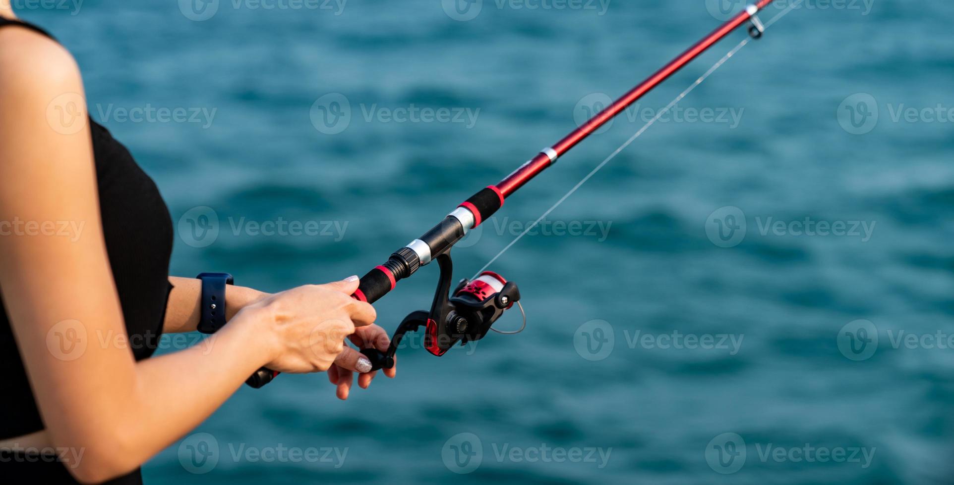 Woman hand holding fishing rod with sea background, fishing at sunset. photo